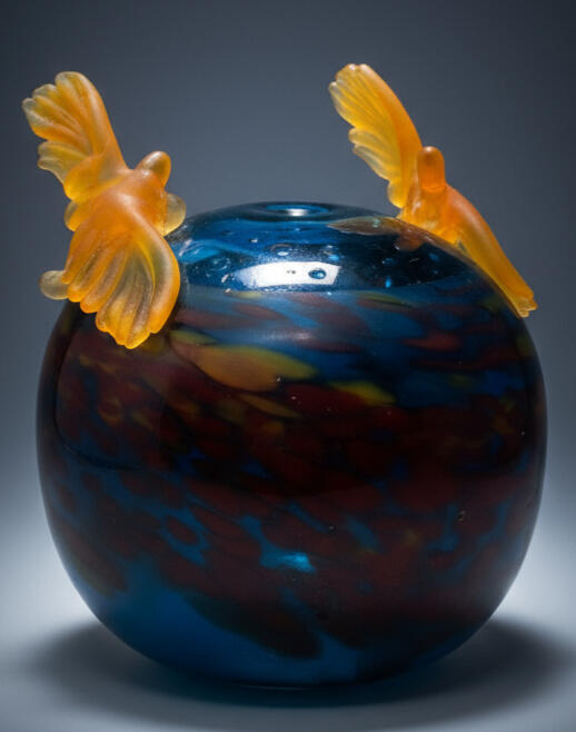 Image of artwork named Kestrel Lufbery which shows two hand sculpted glass kestrels in a lufbery circle around the lip of a blown sphere.