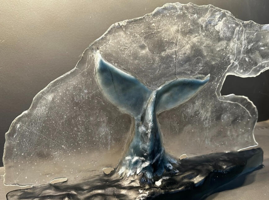 Images of an artwork called The Fluke. It shows a humpback whale's tail breaching the ocean surface against a cloudshaped backdrop. All in cast glass.